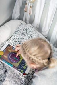Barn ligger i sängen och spelar det pedagogiska spelet Zcooly på iPad